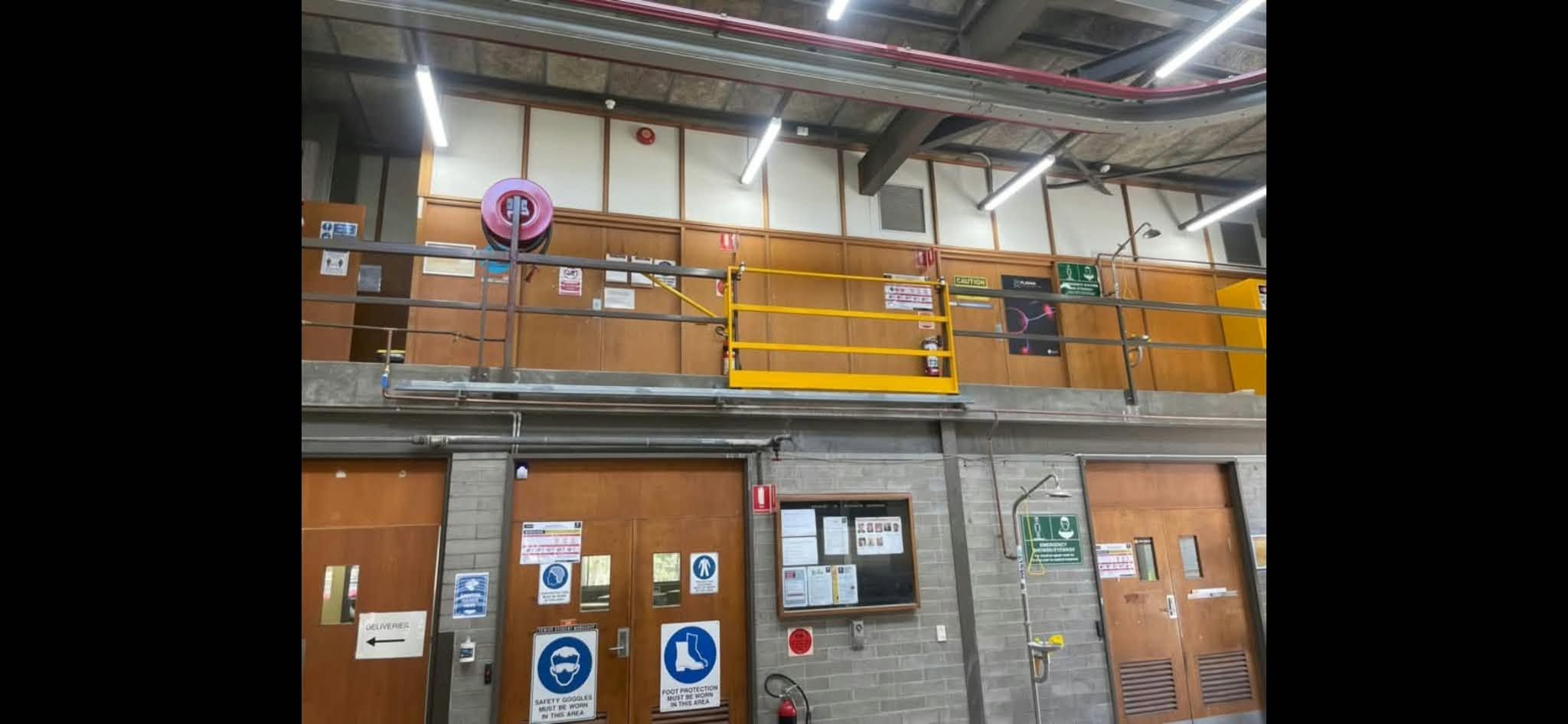 Yellow steel safety gate set into a mezzanine handrail inside a workshop building