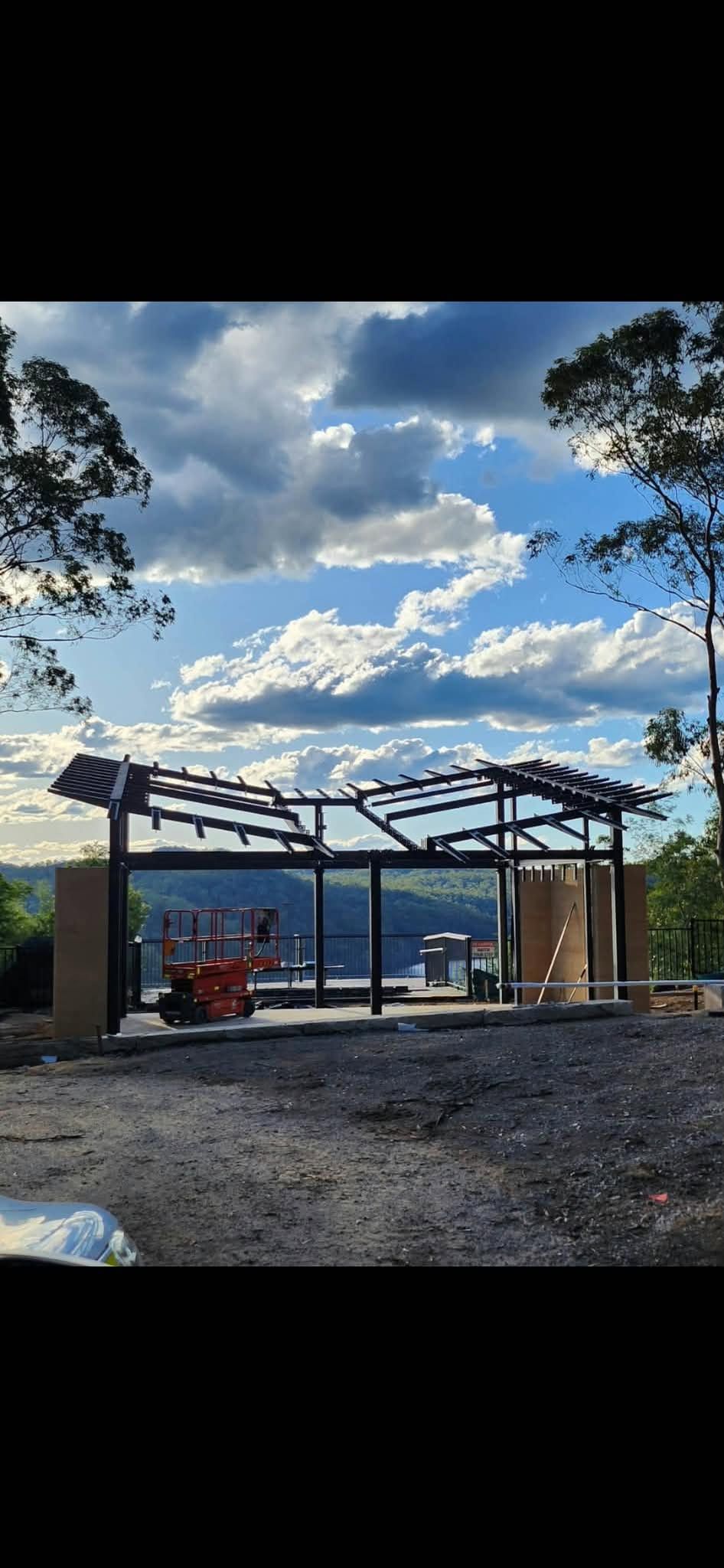 Dark steel frame of the new visitors centre building under construction on a hilltop, with a scissor lift beside it